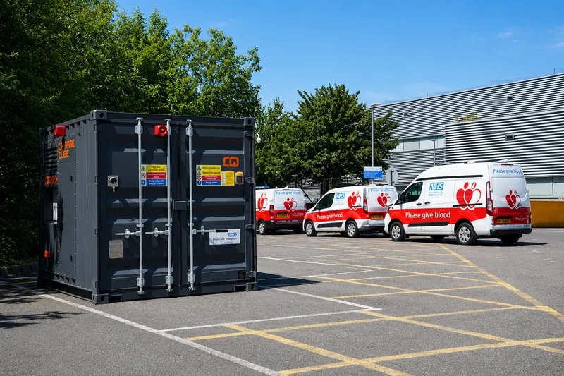 A Charge Qube CQ450 in an NHS Blood and Transplant car park with Please Give Blood vans alongside