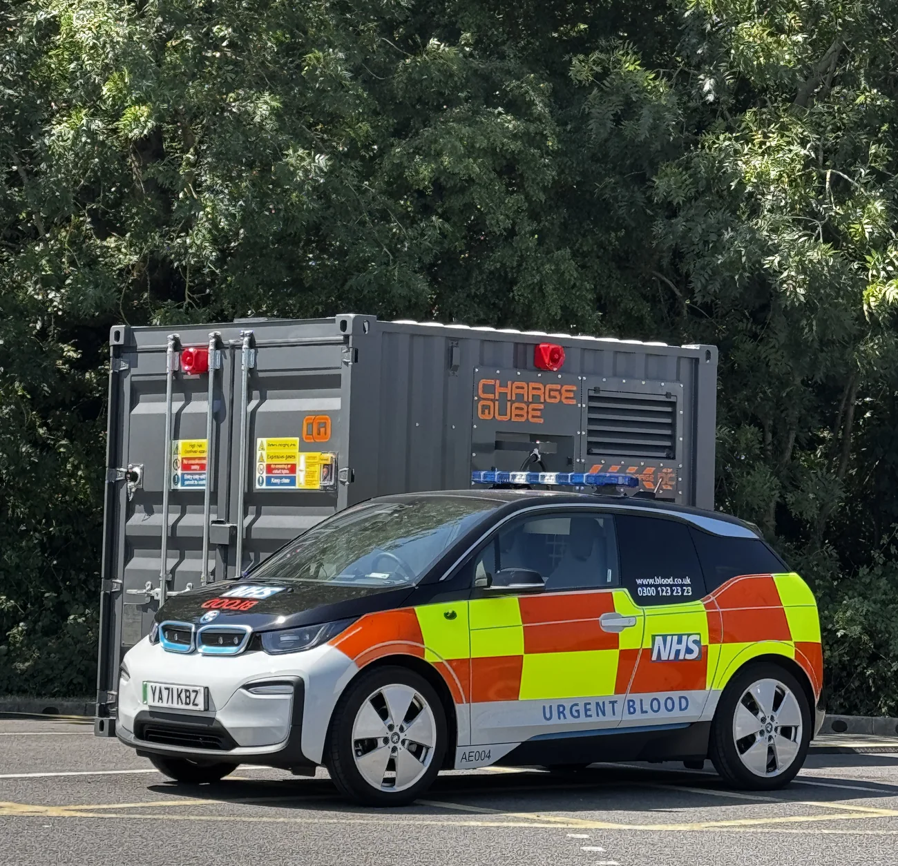 An NHS Urgent Blood response car in blue light livery parked in front of a Charge Qube CQ450 container
